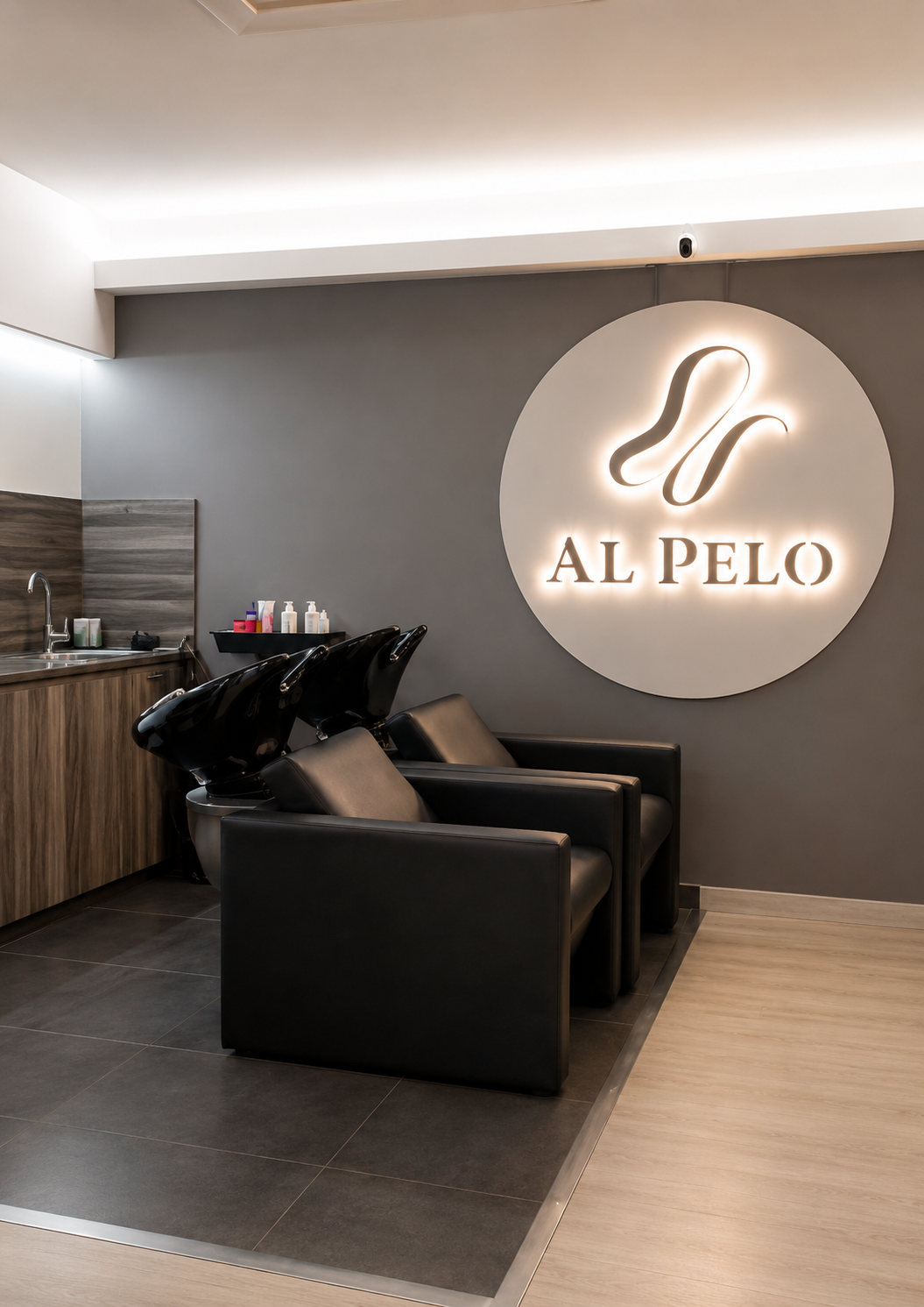 LAVACABEZAS Zona de lavacabezas del salón Al Pelo Perruquers con sillones y logotipo iluminado en la pared